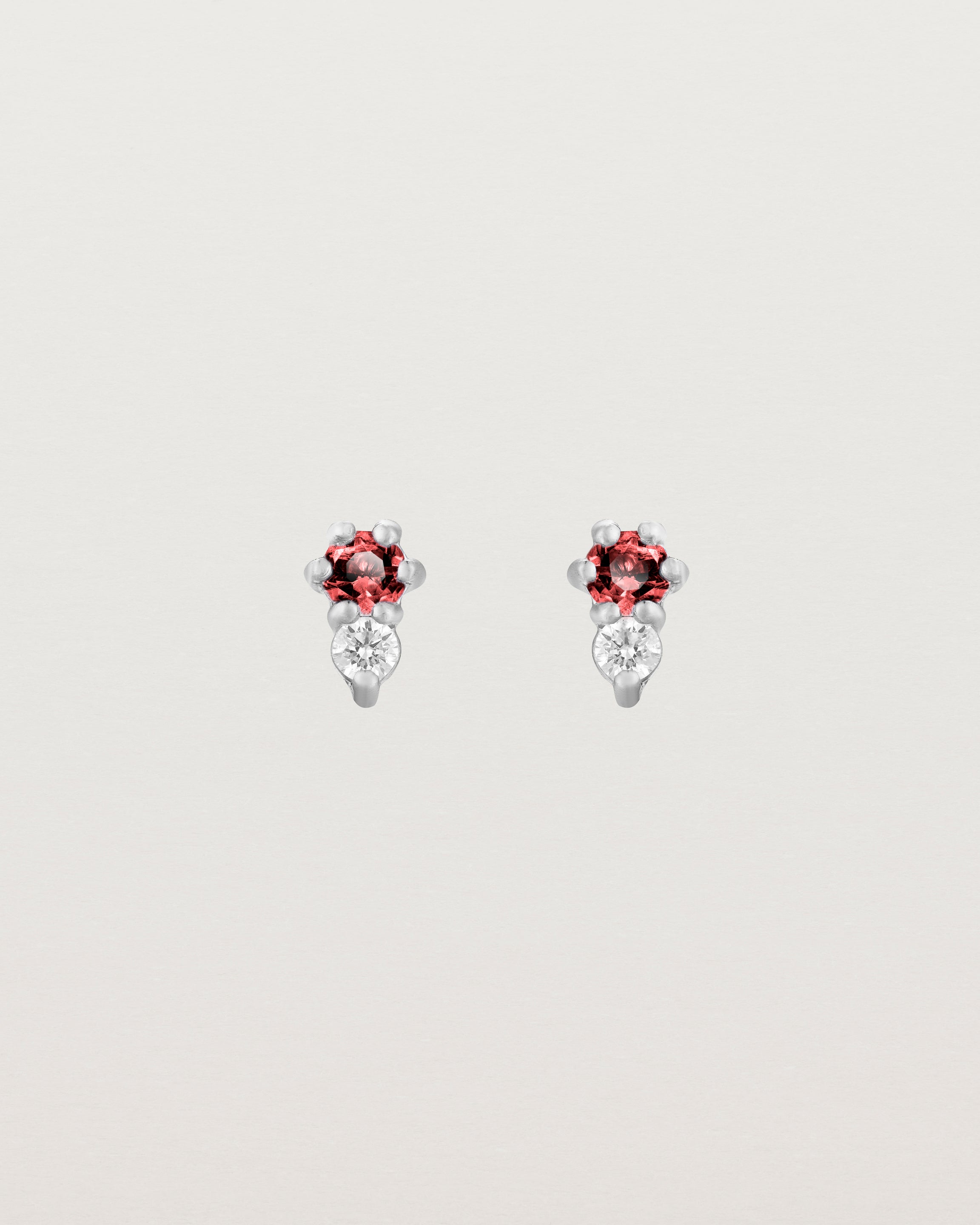 Front facing deep etched image of a pair of white gold earrings with ruby birthstones and diamonds.