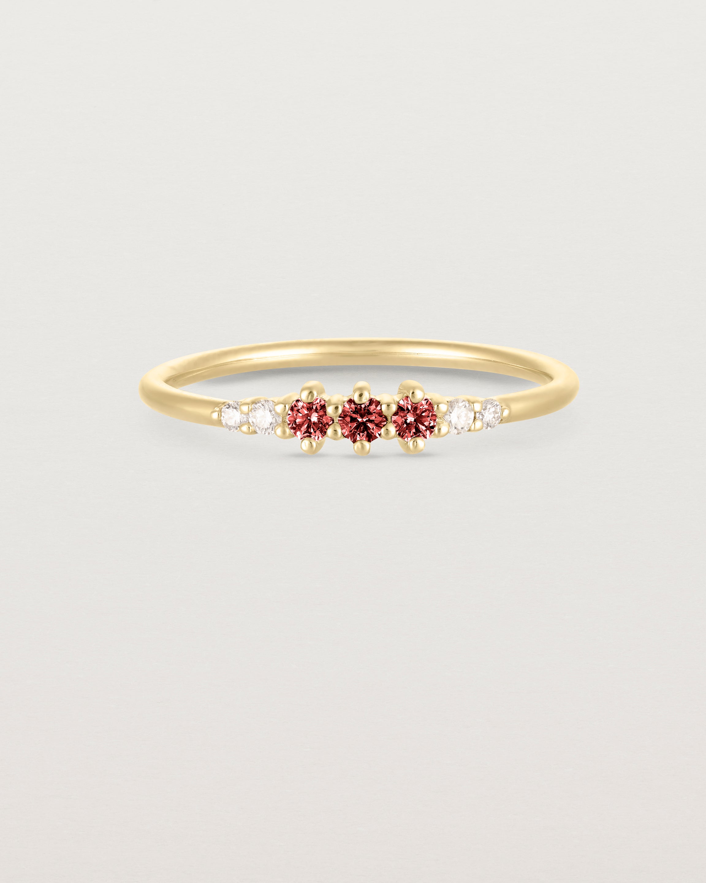 Front facing deep etched image of a yellow gold ring with garnet birthstones and diamonds.