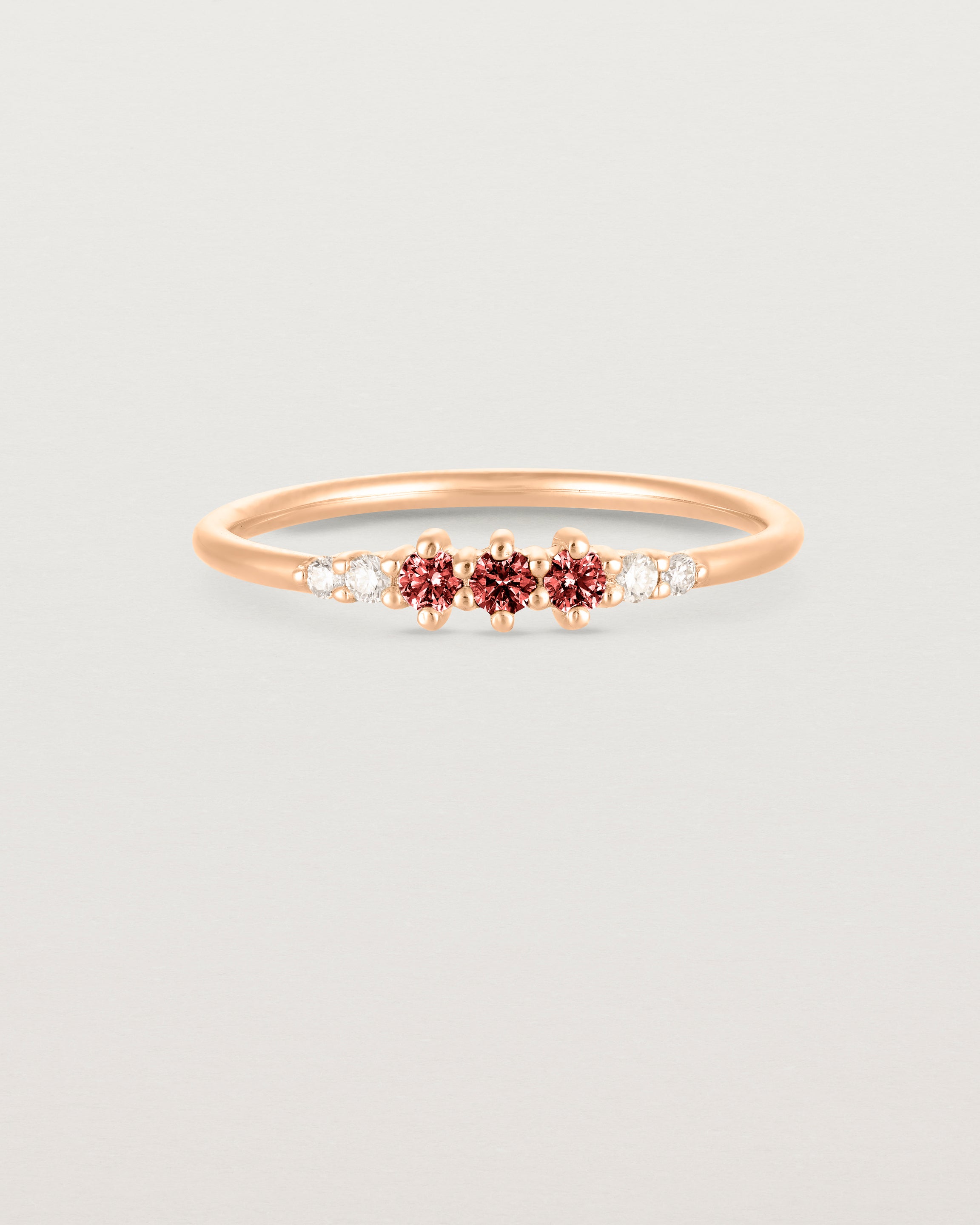 Front facing deep etched image of a rose gold ring with garnet birthstones and diamonds.