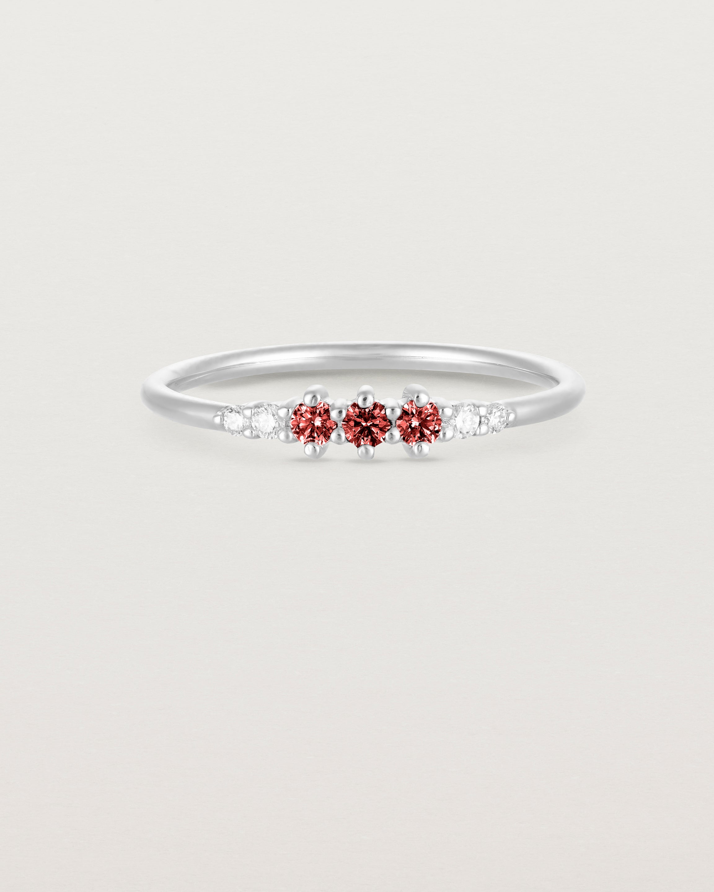 Front facing deep etched image of a white gold ring with garnet birthstones and diamonds.