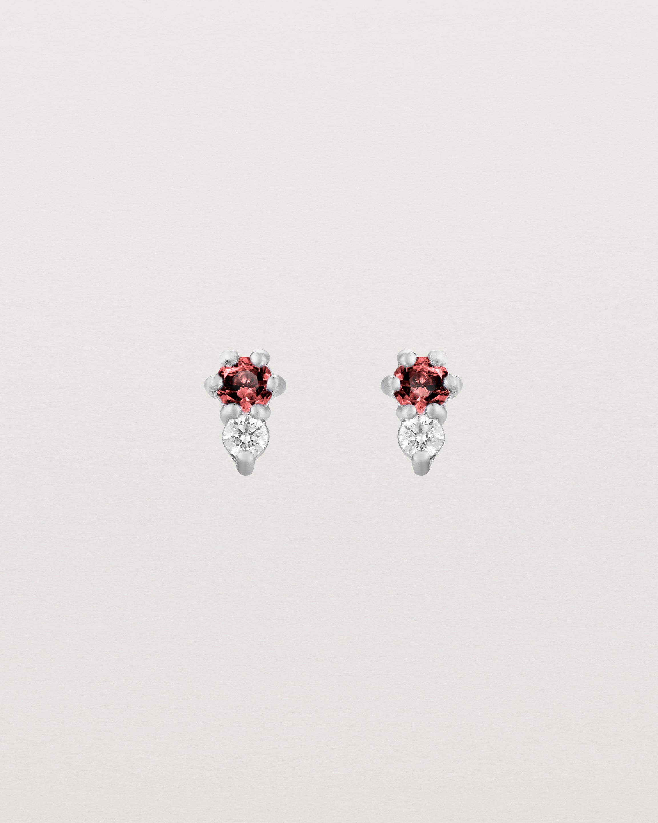 Front facing deep etched image of a pair of white gold earrings with garnet birthstones and diamonds.