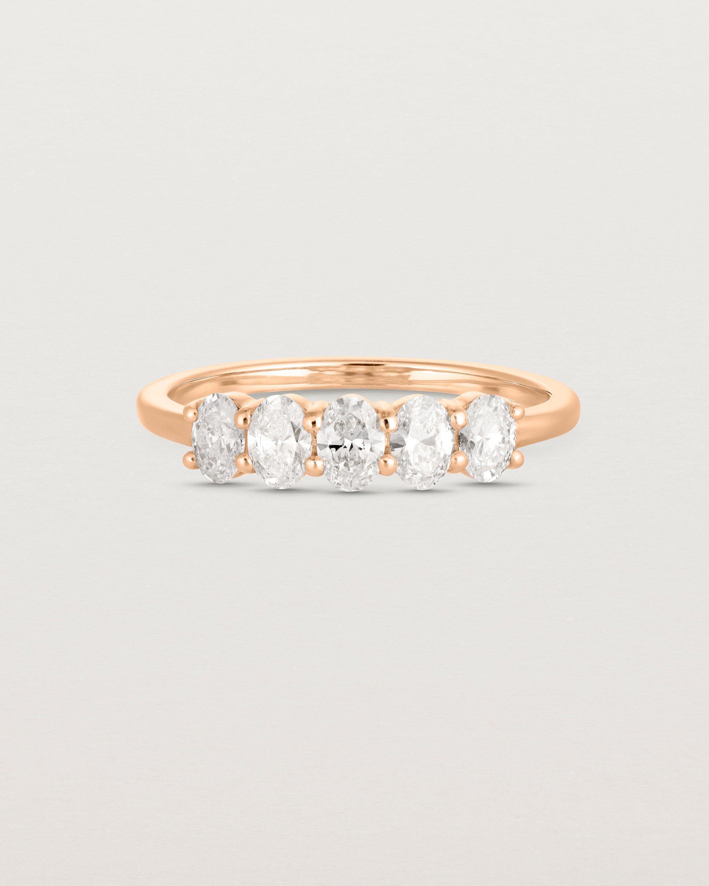 Front on deep etched image of a rose gold wrap engagement ring with five oval diamonds.