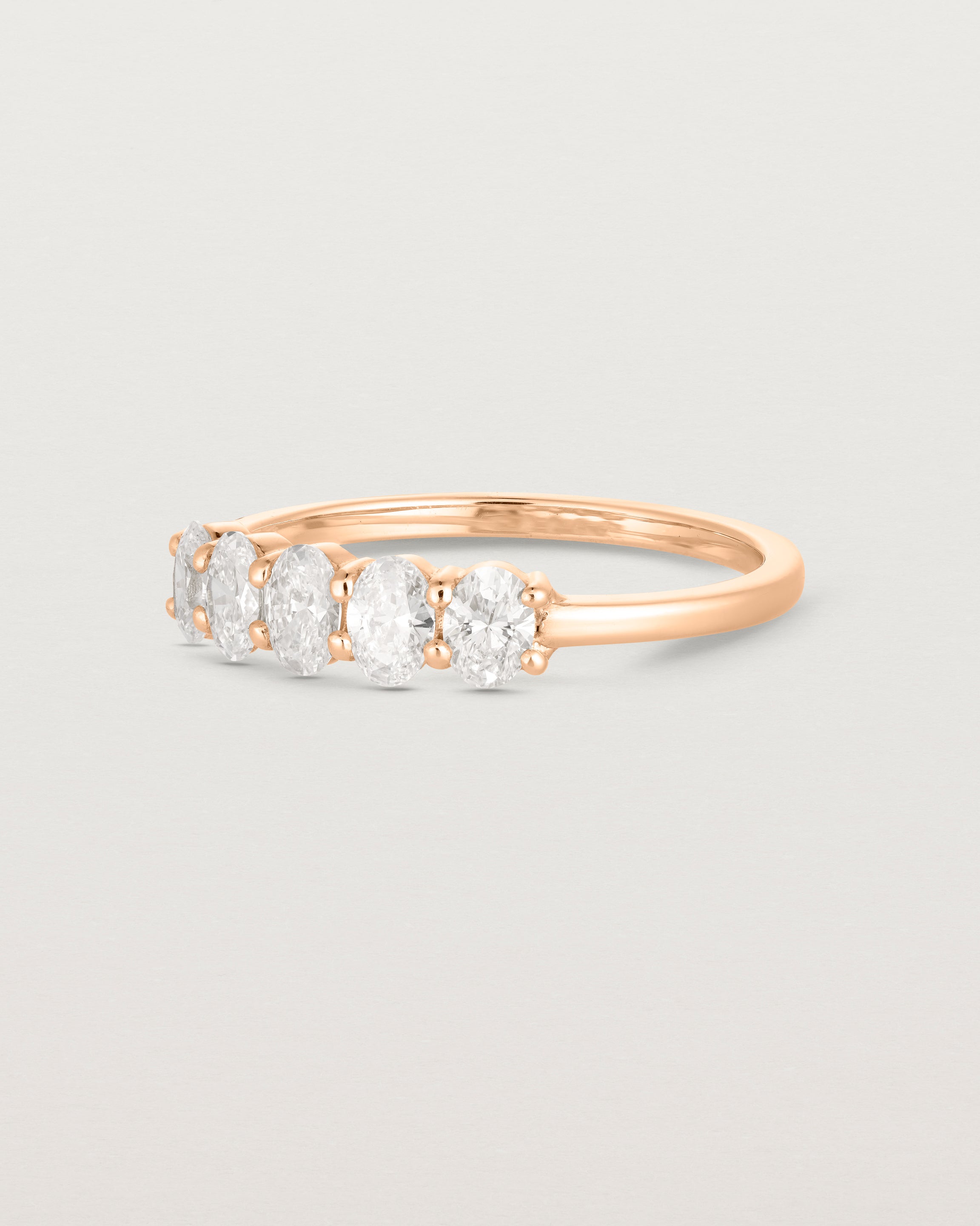 Side on deep etched image of a rose gold wrap engagement ring with five oval diamonds.