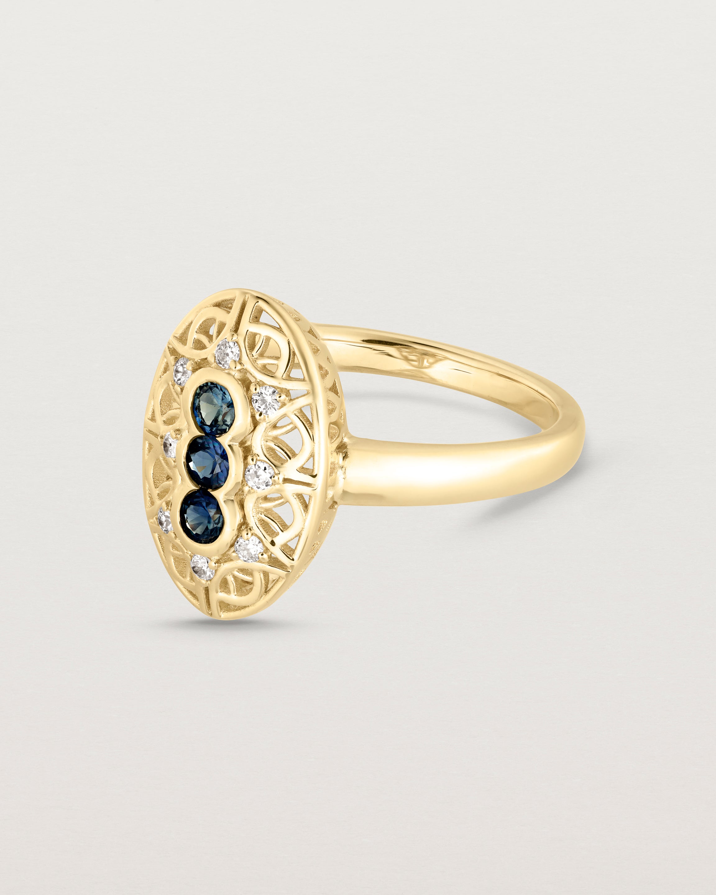 Side facing deep etched image of a yellow gold vintage inspired shield ring with three Australian sapphires and surrounded by eight old cut white diamonds.