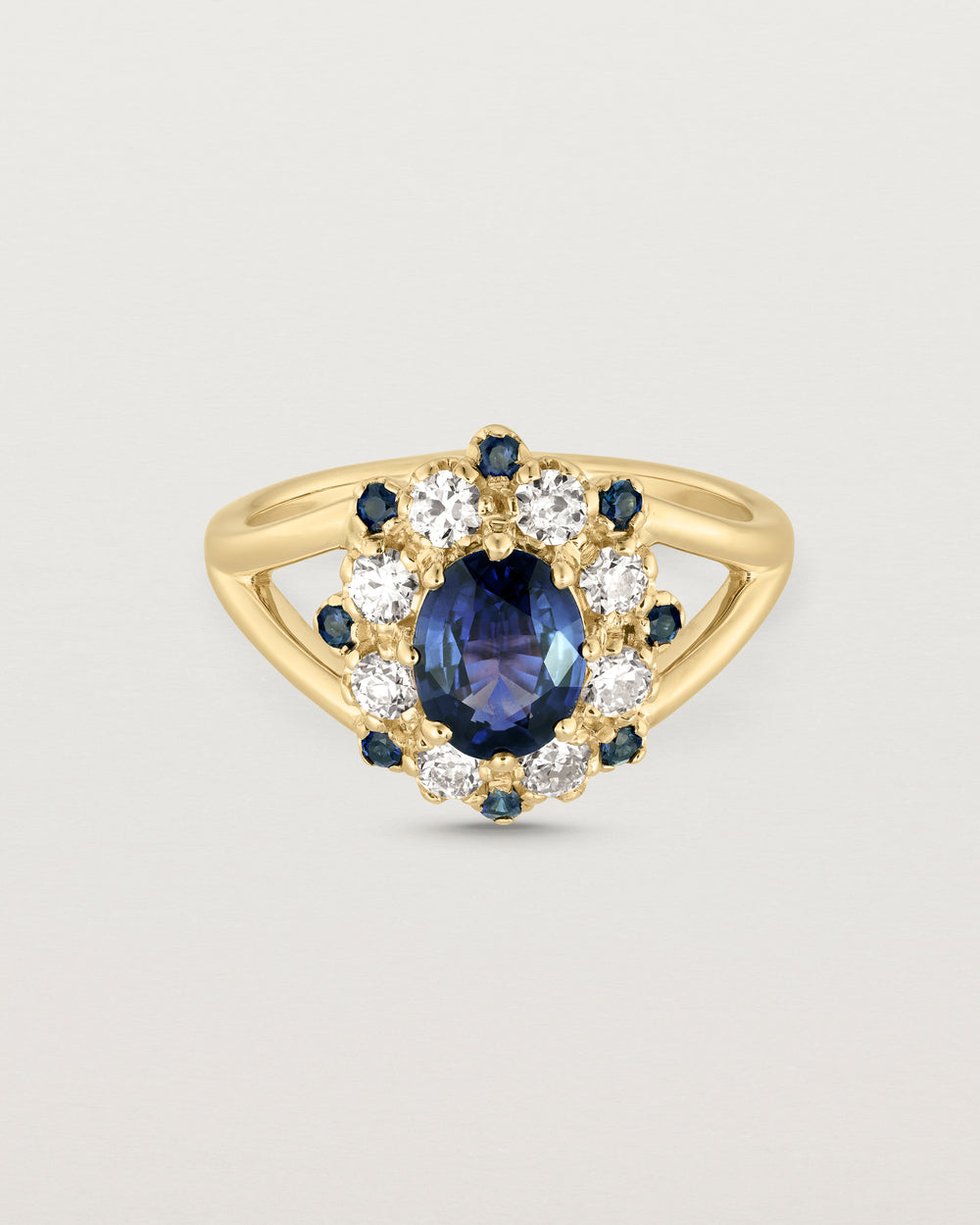 Front facing deep etched image of a yellow gold vintage inspired ring with an oval Ceylon Sapphire and a tiered halo of Old Cut Diamonds and Australian Sapphires.