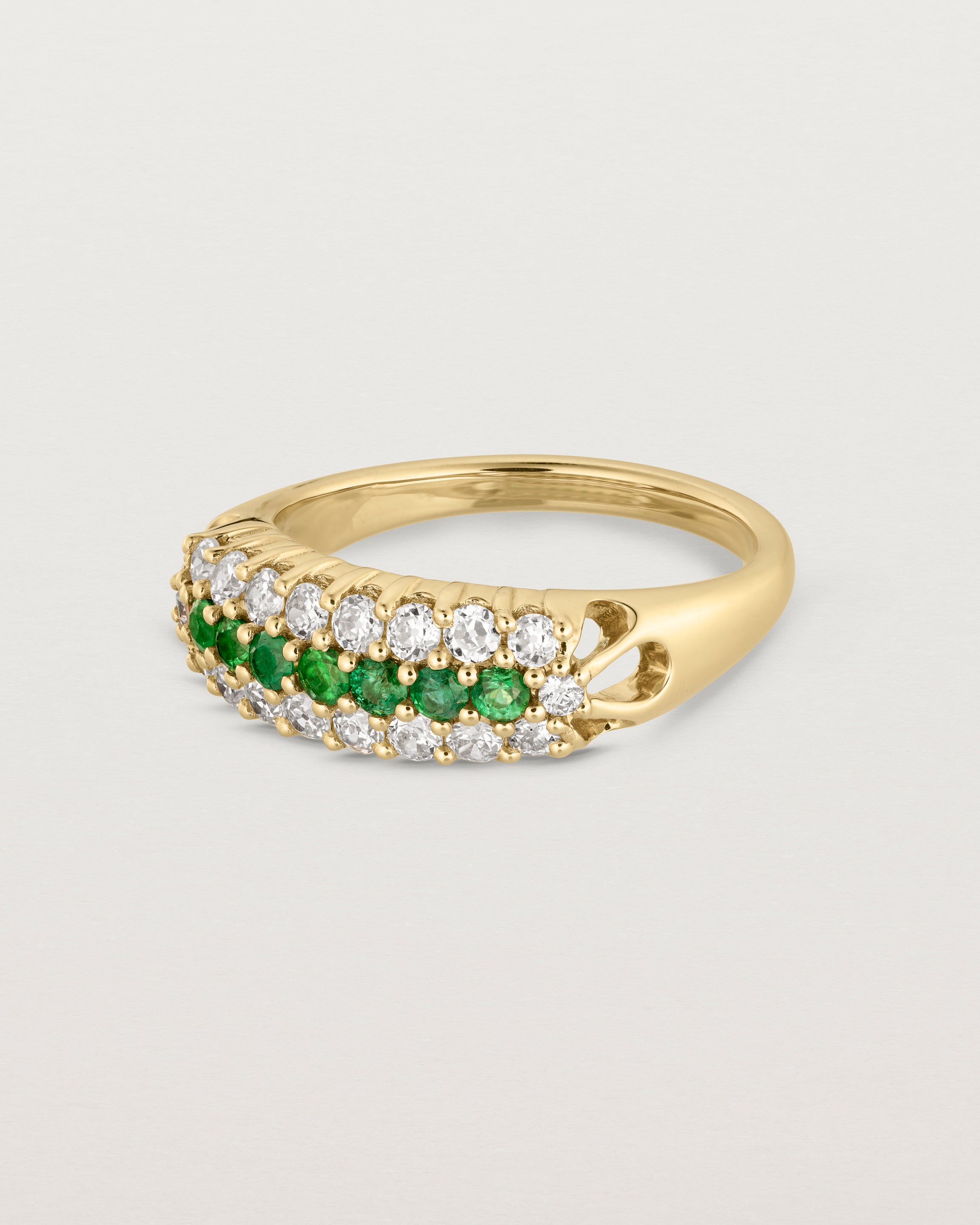 Side facing deep etched image of a yellow gold vintage inspired wrap ring with seven green emeralds and a graduation of 18 old cut diamonds.