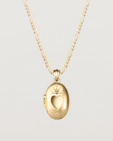 Front facing deep etched image of a yellow gold chain with locket featuring intricate engraving framing a heart shaped window into the locket.