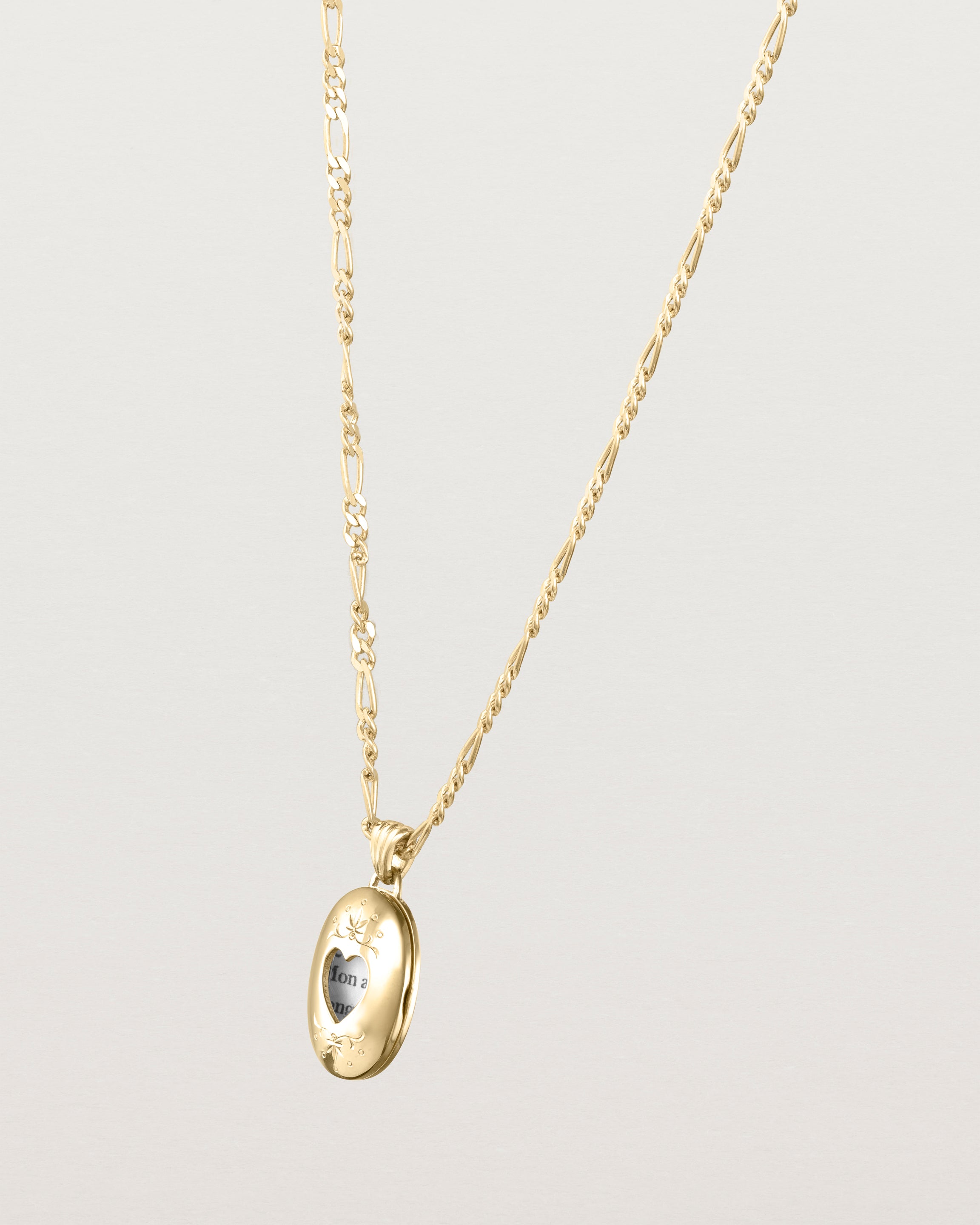 Side facing deep etched image of a yellow gold chain with locket featuring intricate engraving framing a heart shaped window into the locket.