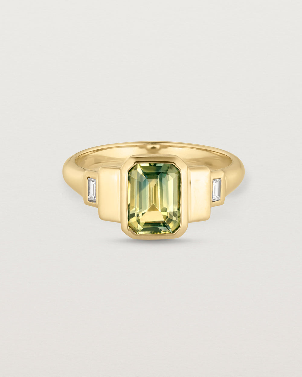 Front facing deep etched image of a yellow gold vintage inspired ring with an emerald cut African parti sapphire with graduating layers either side of the central stone and two white diamond baguettes.