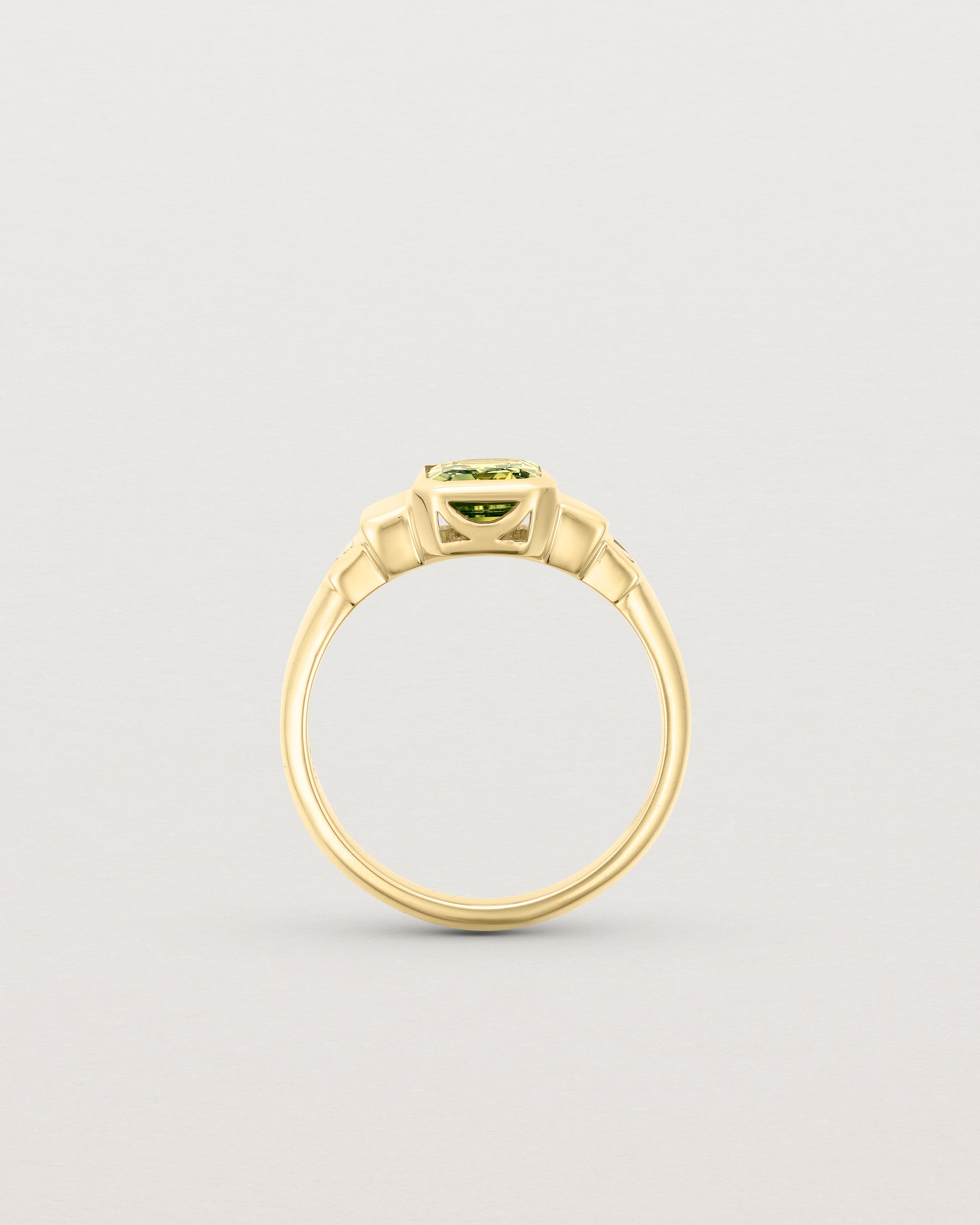 Standing deep etched image of a yellow gold vintage inspired ring with an emerald cut African parti sapphire with graduating layers either side of the central stone and two white diamond baguettes.