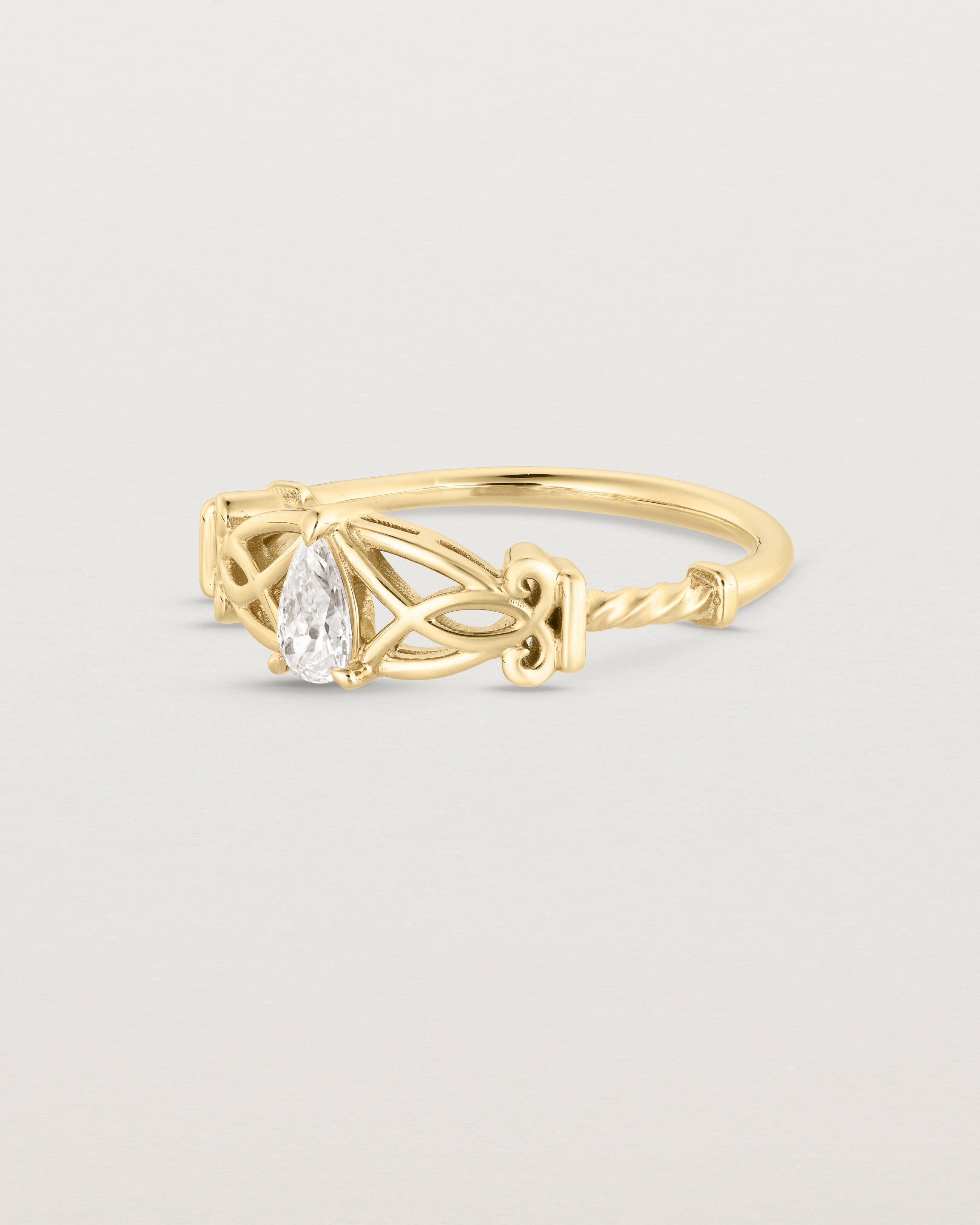 Side facing deep etched image of a vintage inspired yellow gold ring with an old mine cut pear diamond and intricate wire work.