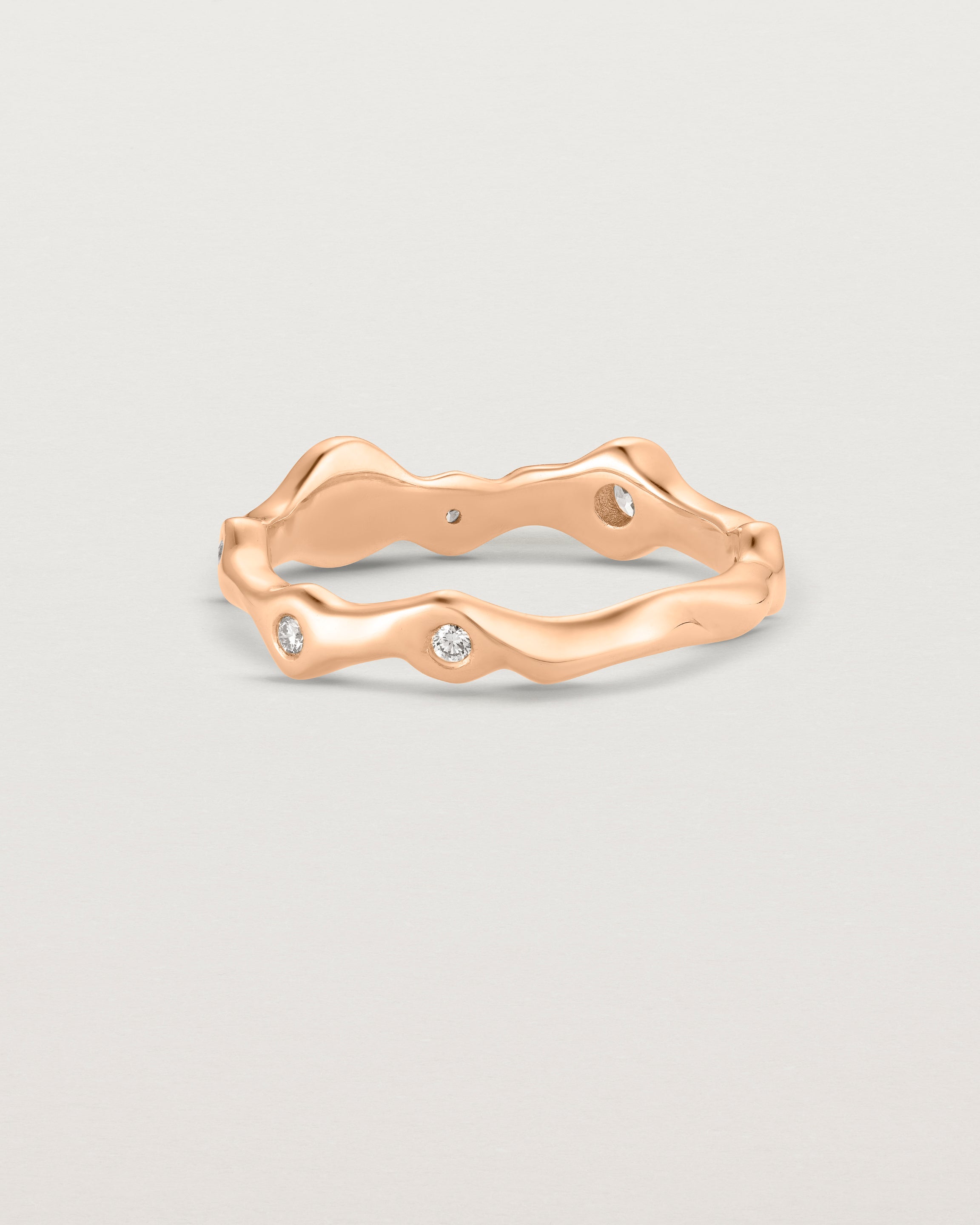 Back facing deep etched image of a rose gold ring with seven scattered white diamonds.