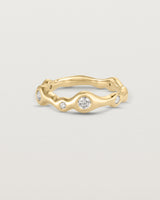 Front on deep etched image of a yellow gold ring with seven scattered white diamonds.
