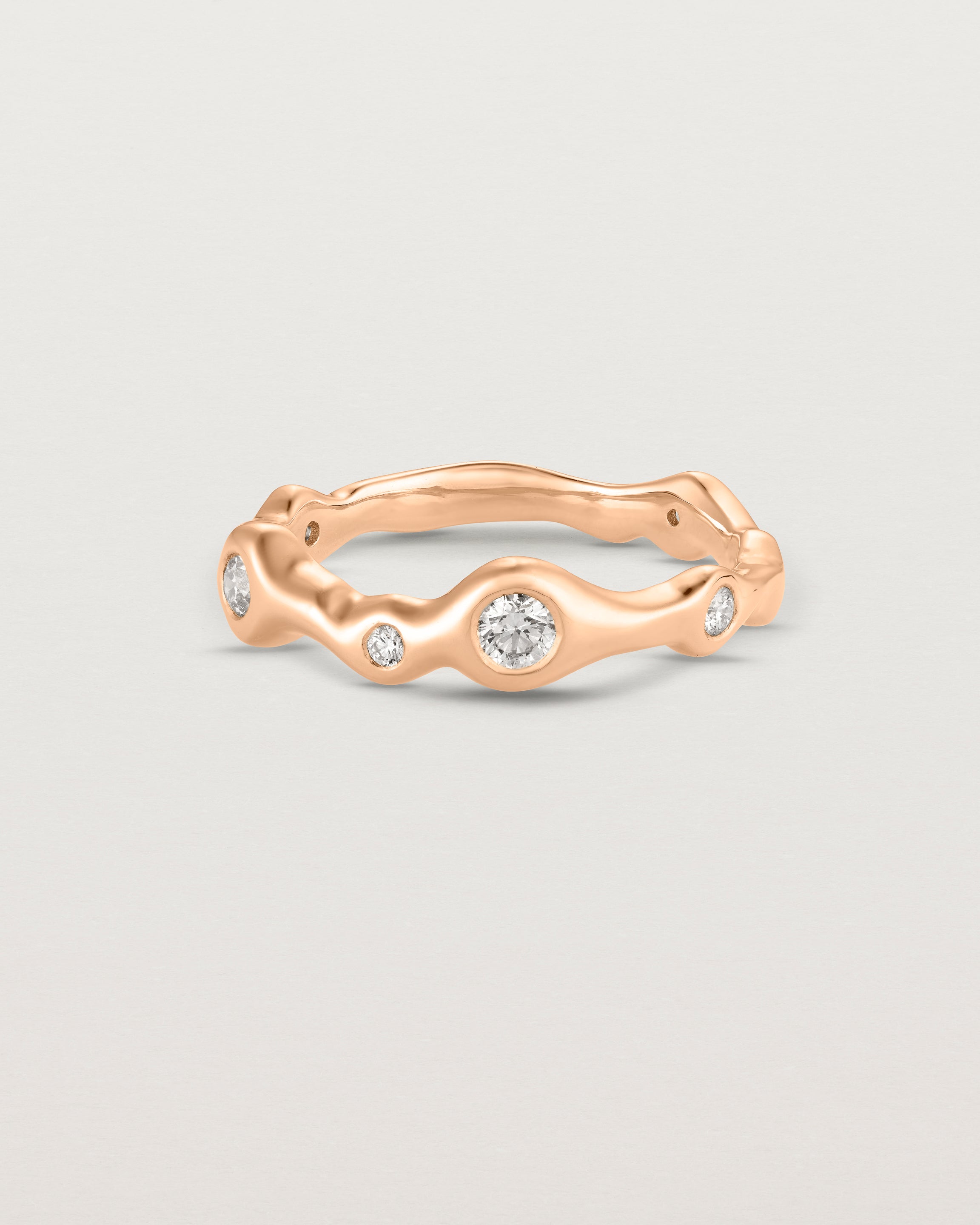 Front on deep etched image of a rose gold ring with seven scattered white diamonds.