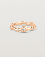 Front on deep etched image of a rose gold ring with seven scattered white diamonds.