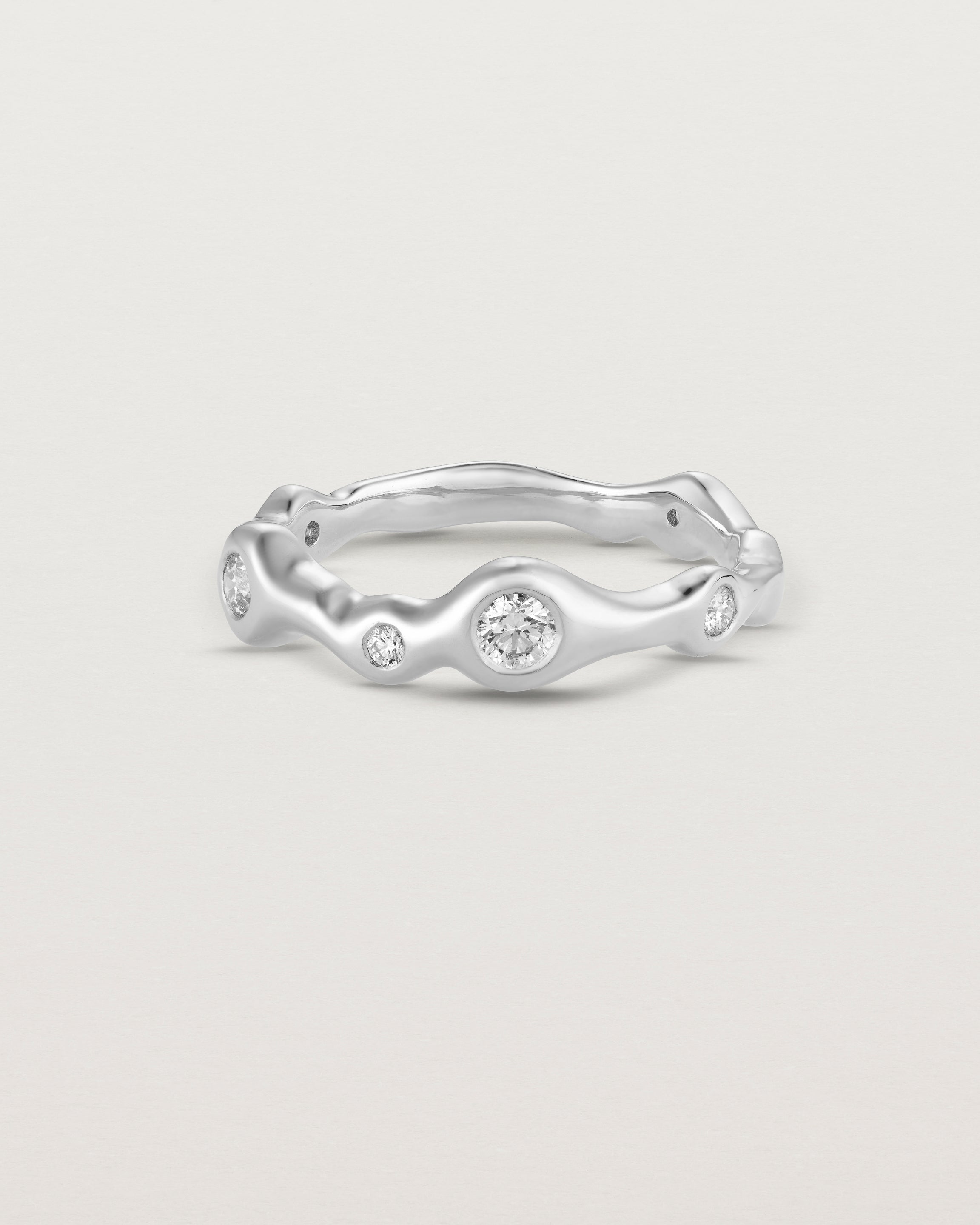 Front on deep etched image of a white gold ring with seven scattered white diamonds.