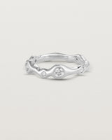 Front on deep etched image of a white gold ring with seven scattered white diamonds.