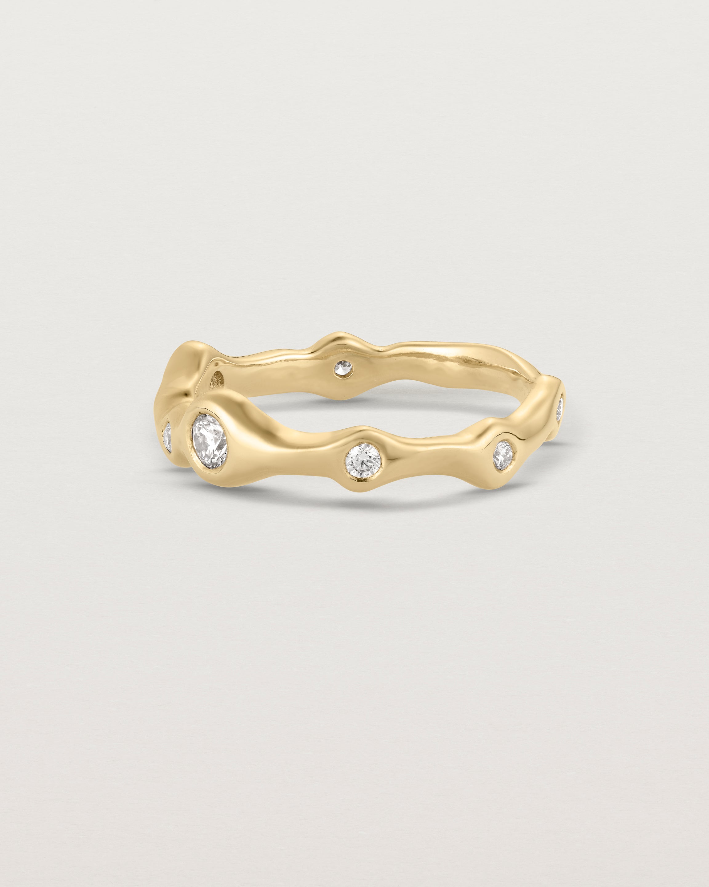 Side facing deep etched image of a yellow gold ring with seven scattered white diamonds.