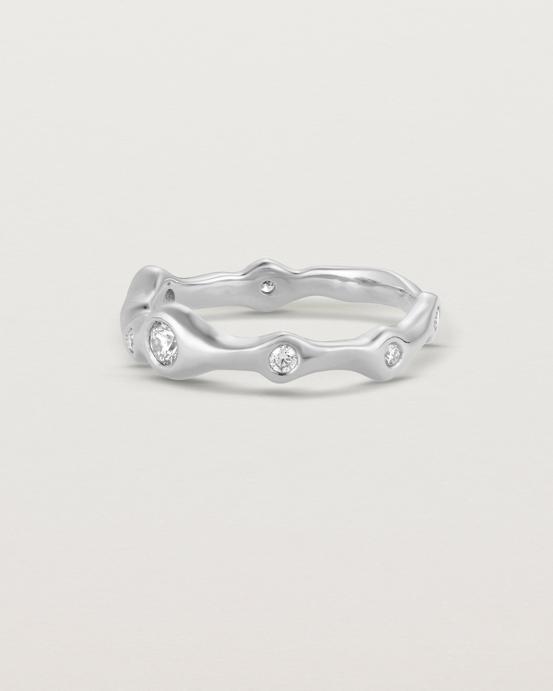 Side facing deep etched image of a white gold ring with seven scattered white diamonds.