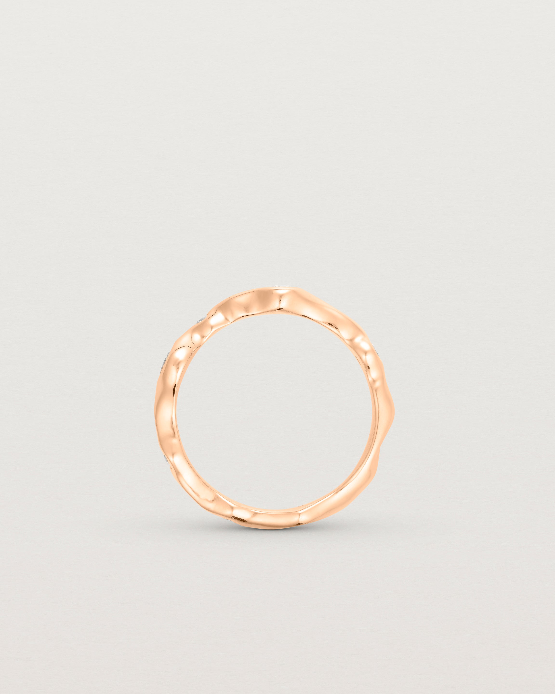 Standing deep etched image of a rose gold ring with seven scattered white diamonds.