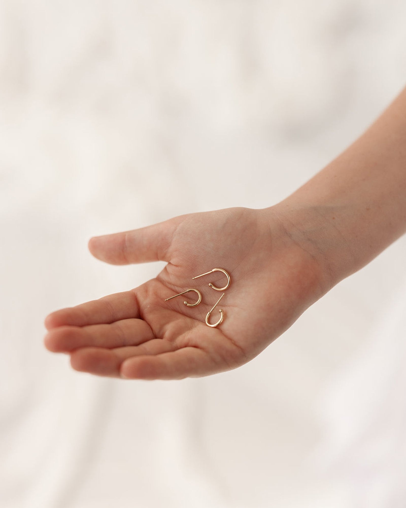 three different sizes in the hands of a child model showing the suspend hoops in yellow gold