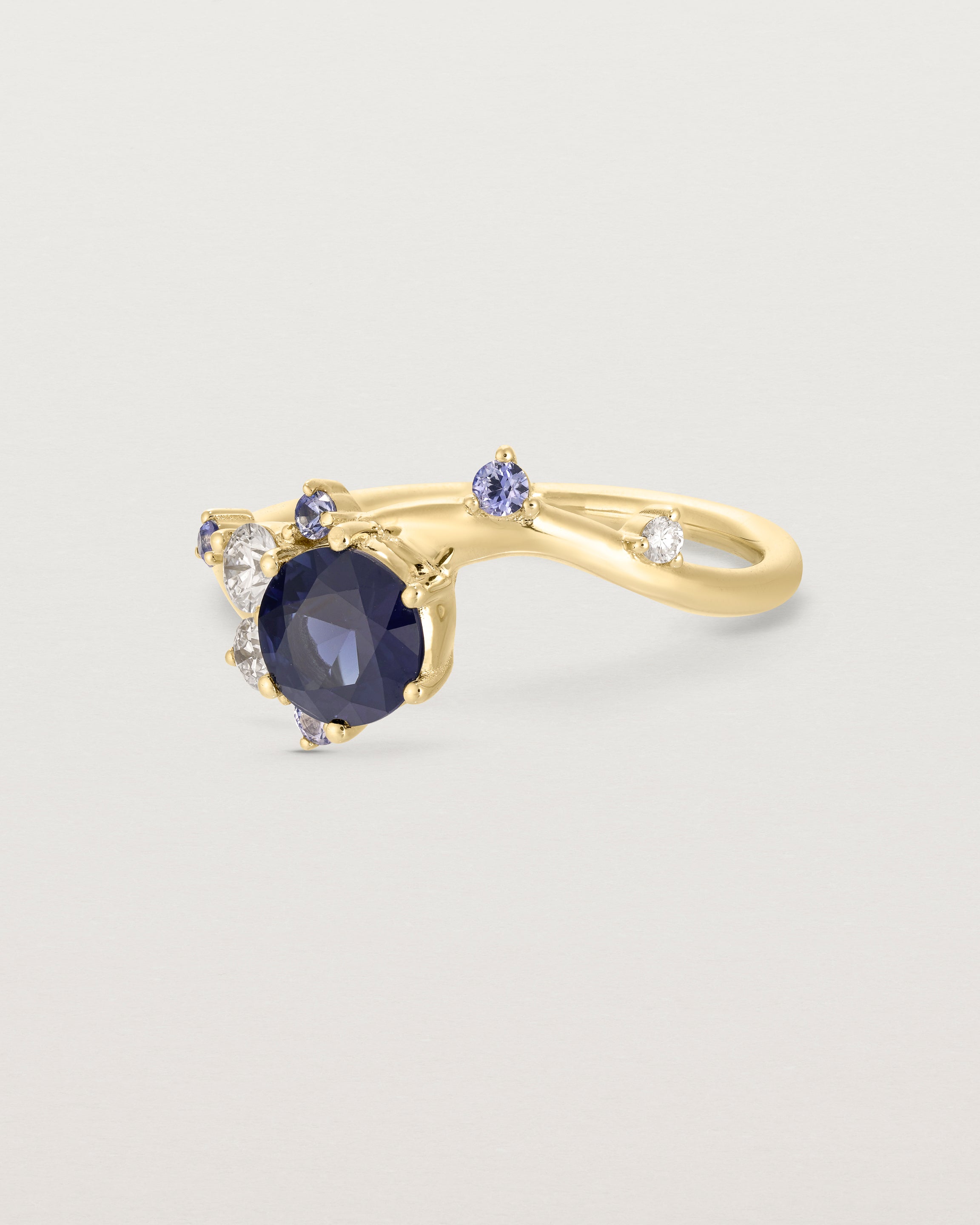 side facing deep etched image of a yellow gold  engagement ring with a cluster of laboratory grow diamonds and a centre sapphire stone