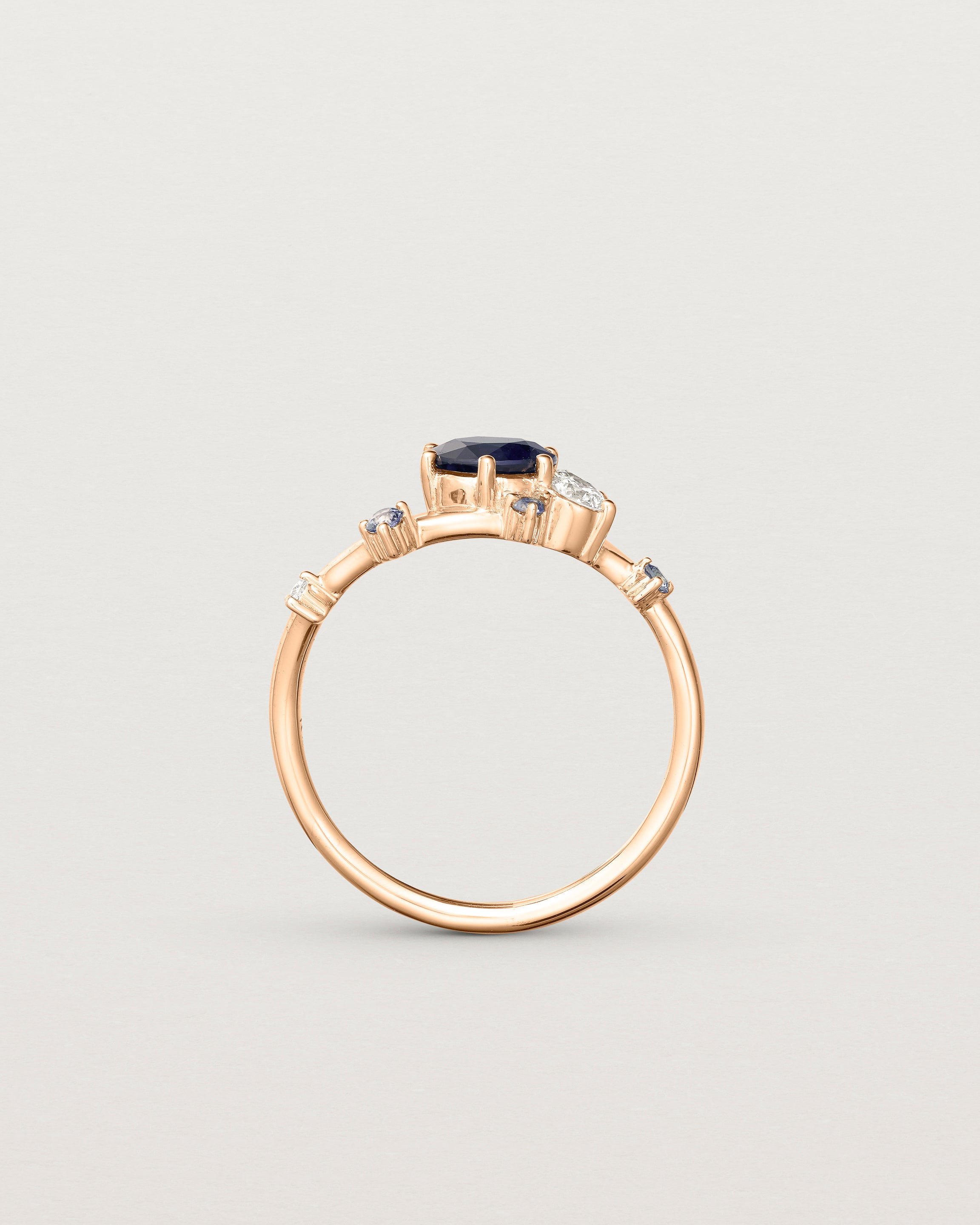 standing deep etched image of a rose gold  engagement ring with a cluster of laboratory grow diamonds and a centre sapphire stone