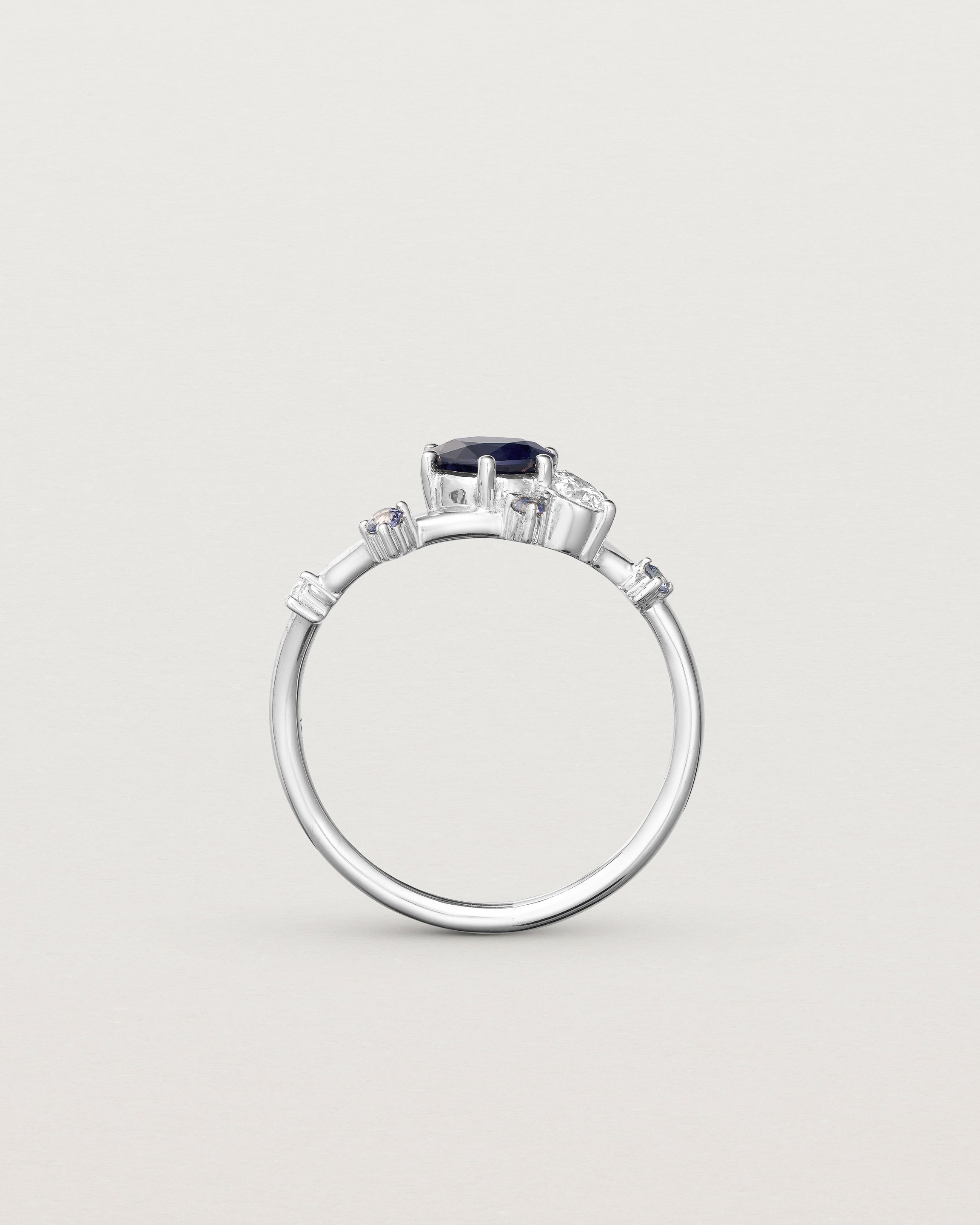 standing deep etched image of a white gold  engagement ring with a cluster of laboratory grow diamonds and a centre sapphire stone