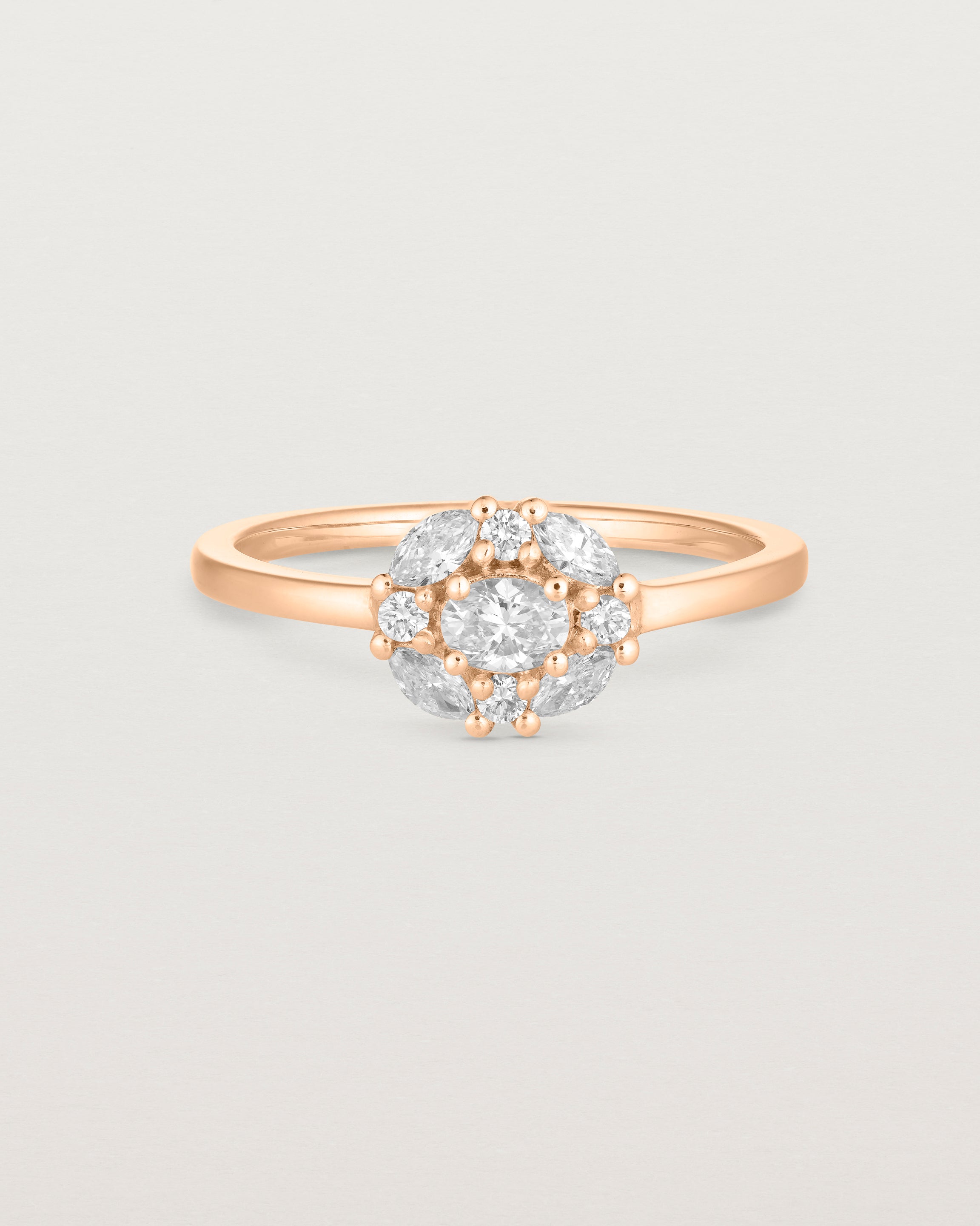 Front on deep etched image of a rose gold engagement ring with an oval white diamond and a halo of eight diamonds.