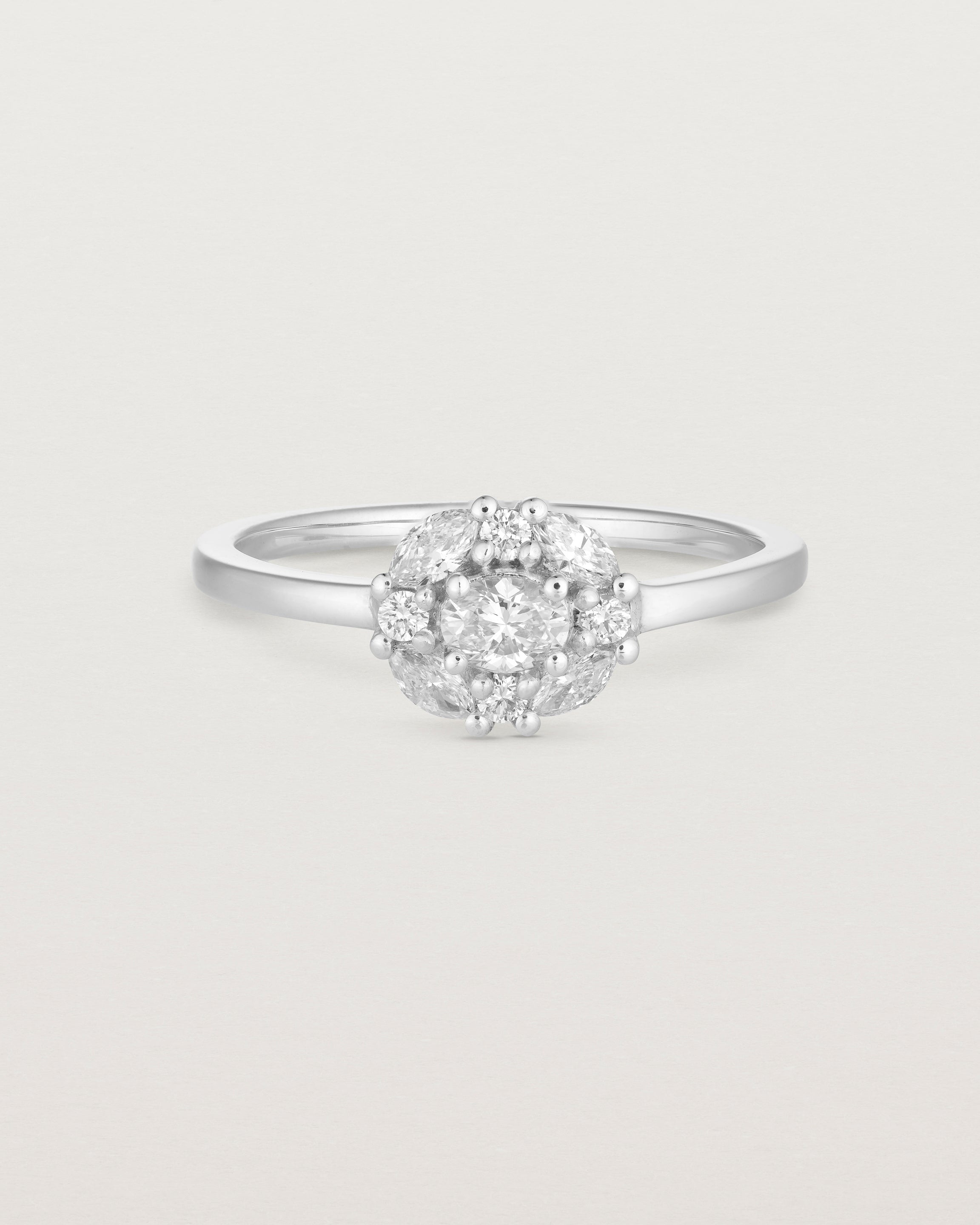 Front on deep etched image of a white gold engagement ring with an oval white diamond and a halo of eight diamonds.