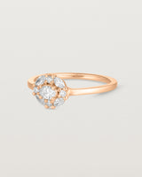 Side on deep etched image of a rose gold engagement ring with an oval white diamond and a halo of eight diamonds.