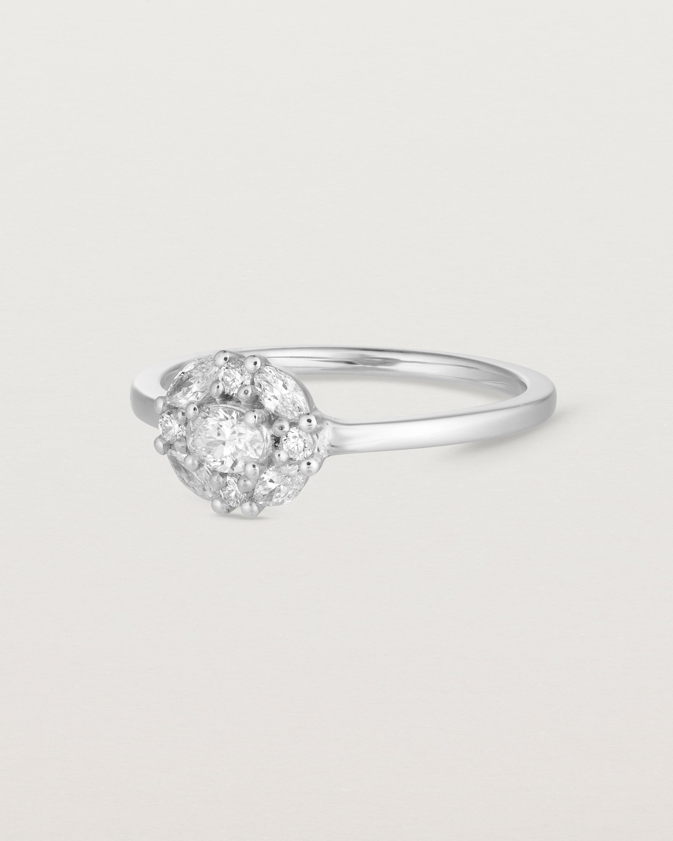 Side on deep etched image of a white gold engagement ring with an oval white diamond and a halo of eight diamonds.