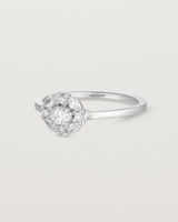 Side on deep etched image of a white gold engagement ring with an oval white diamond and a halo of eight diamonds.