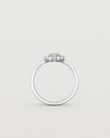 Standing image of a  deep etched image of a white gold engagement ring with an oval white diamond and a halo of eight diamonds.