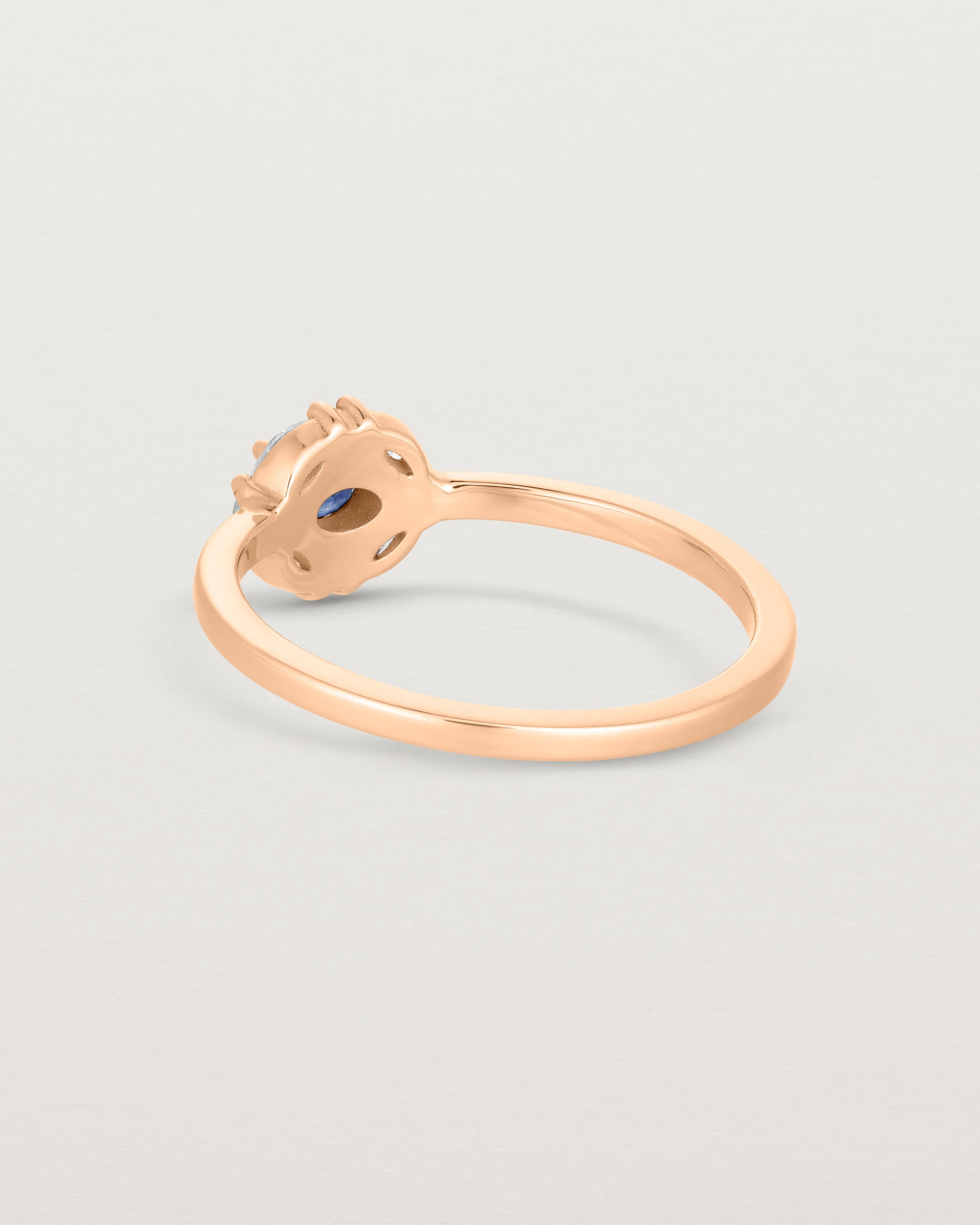 Back facing deep etched image of a rose gold engagement ring with an oval white diamond and a halo of eight diamonds.