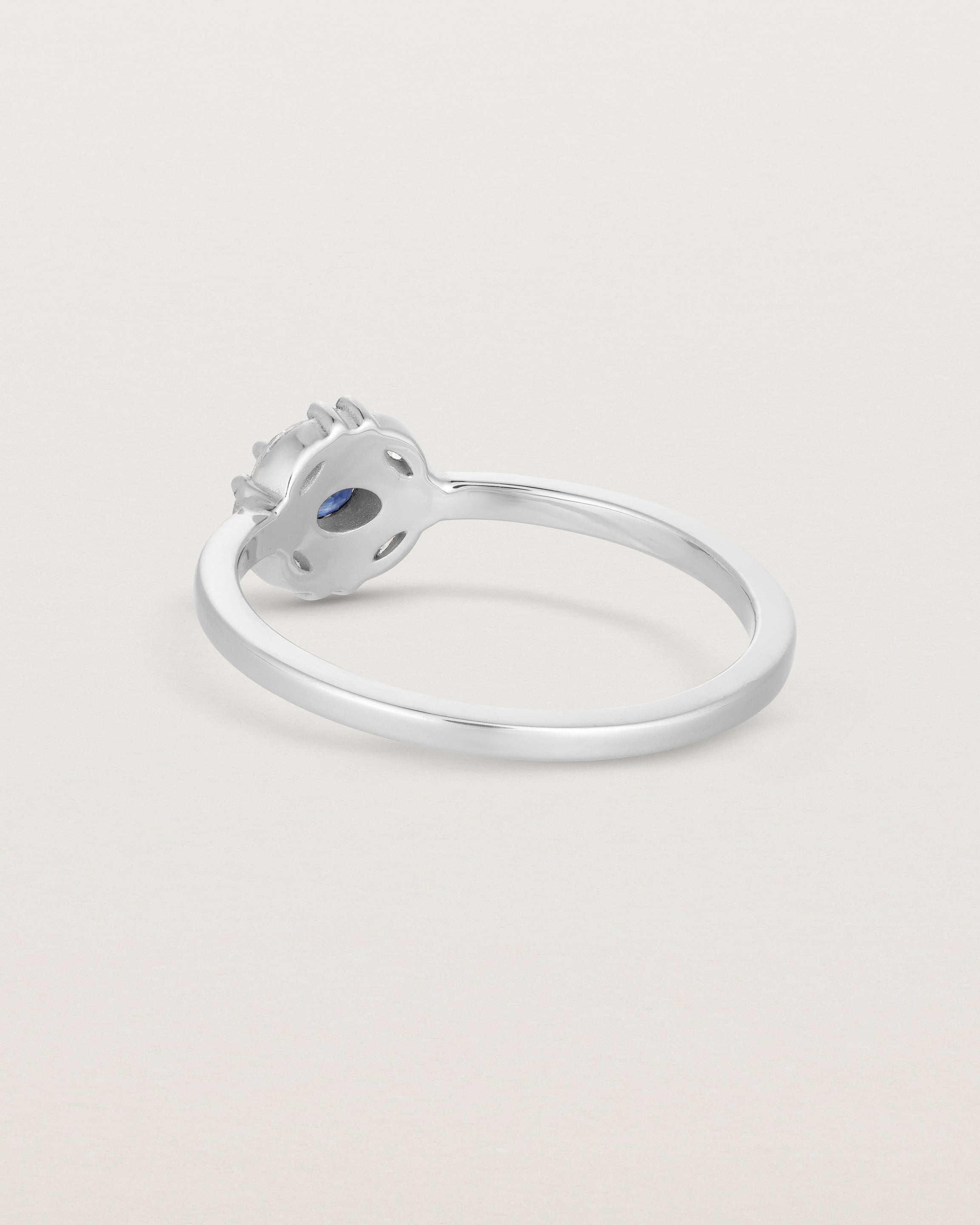 Back facing etched image of a white engagement ring with an oval sapphire stone and a halo of eight diamonds.