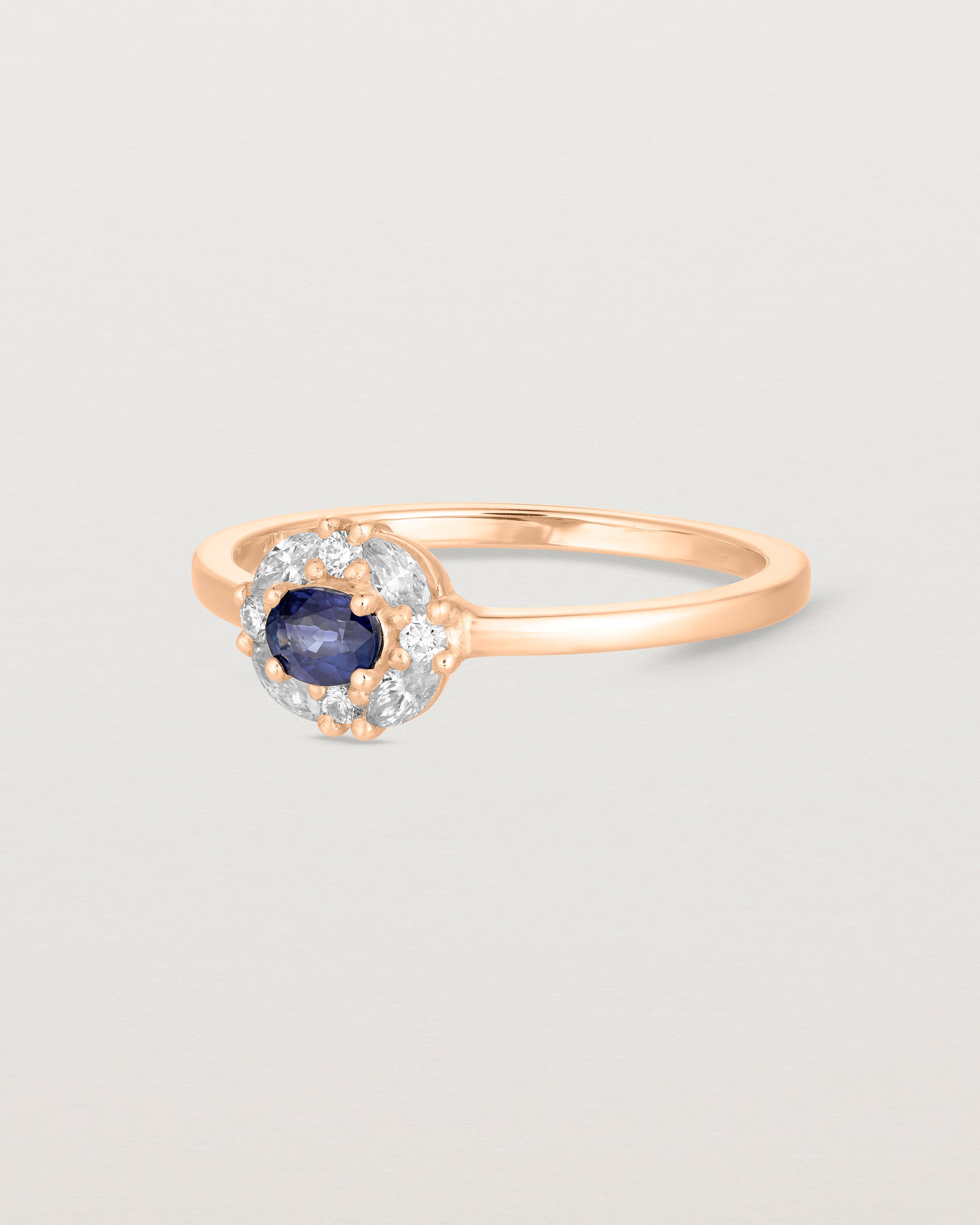 Side on deep etched image of a rose gold engagement ring with an oval white diamond and a halo of eight diamonds.