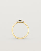 standing view of a deep etched image of a yellow gold engagement ring with an oval sapphire stone and a halo of eight diamonds.