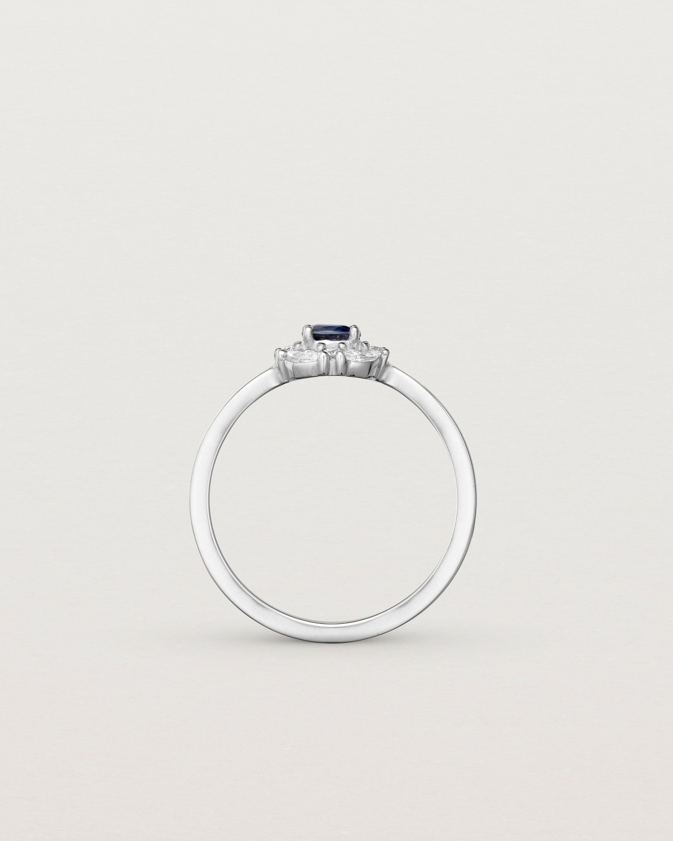 Standing deep etched image of a white engagement ring with an oval sapphire stone and a halo of eight diamonds.